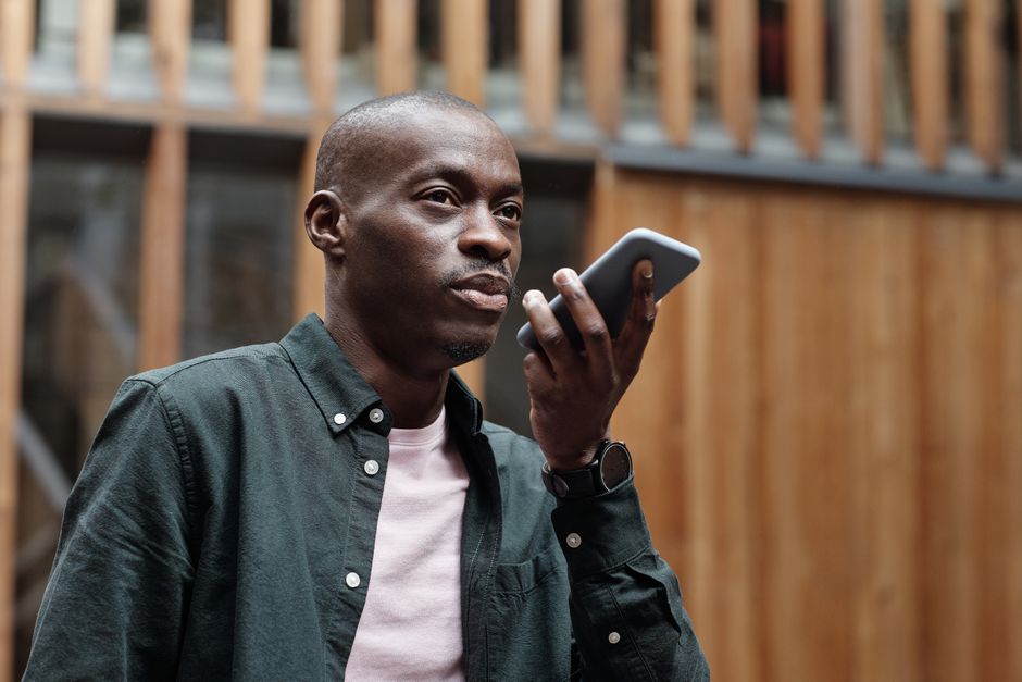 Homem adulto estiloso usando seu smartphone para comandos de voz em um ambiente urbano ao ar livre.
