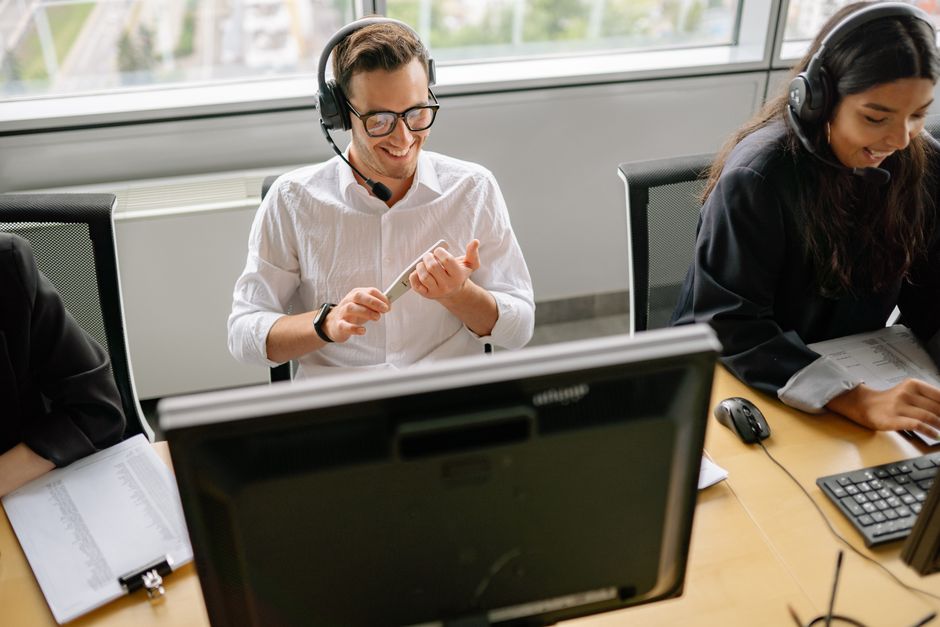 Colegas trabalhando em uma mesa com computadores e fones de ouvido em um escritório moderno.